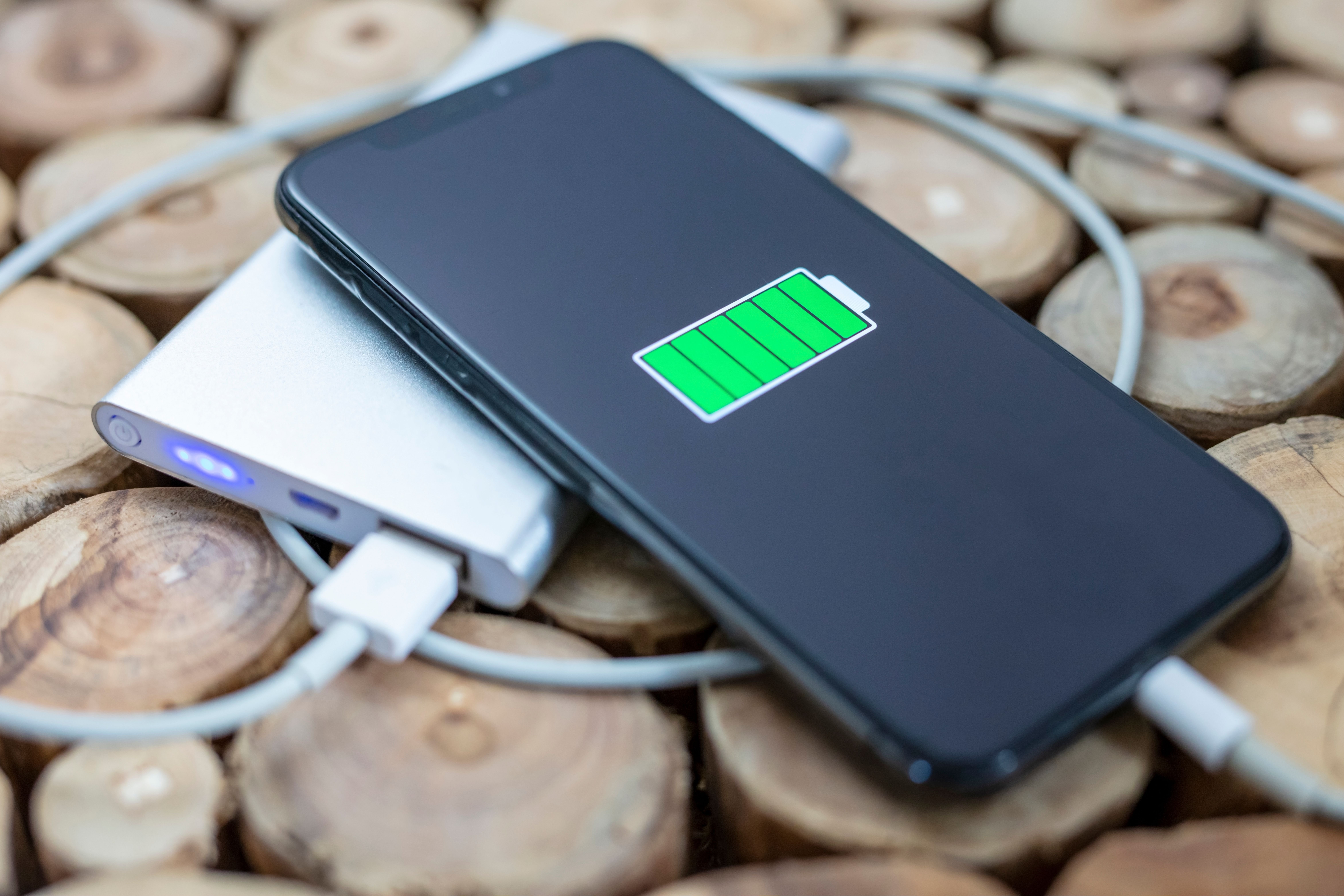 Smartphone charging on a portable power bank with a full green battery icon displayed on the screen.